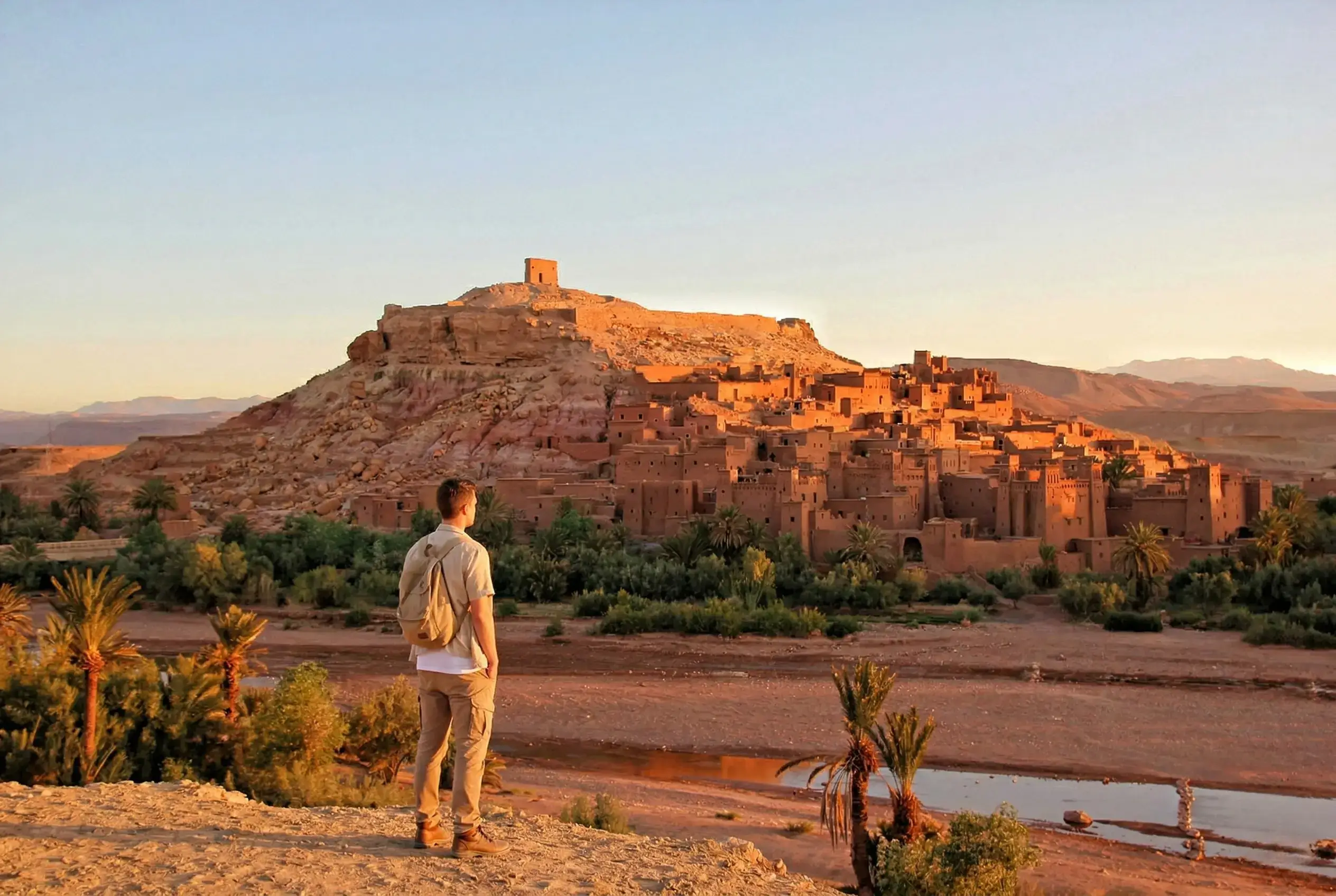 Ait Ben Haddou kasbah during a day trip from Marrakech with palm trees and desert landscape at sunset.