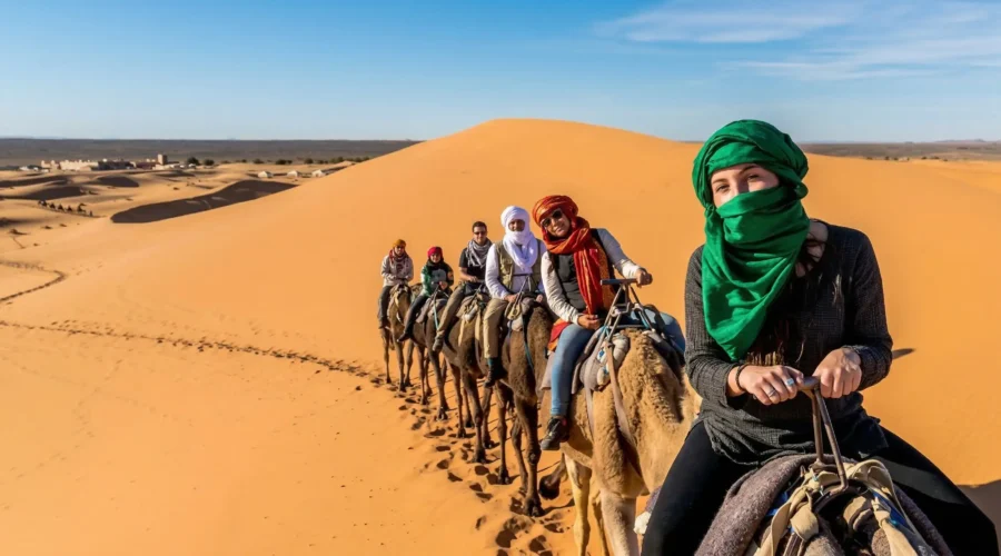 Travelers riding camels across the Erg Chebbi dunes during a 3 days Marrakech to Merzouga desert tour in Morocco