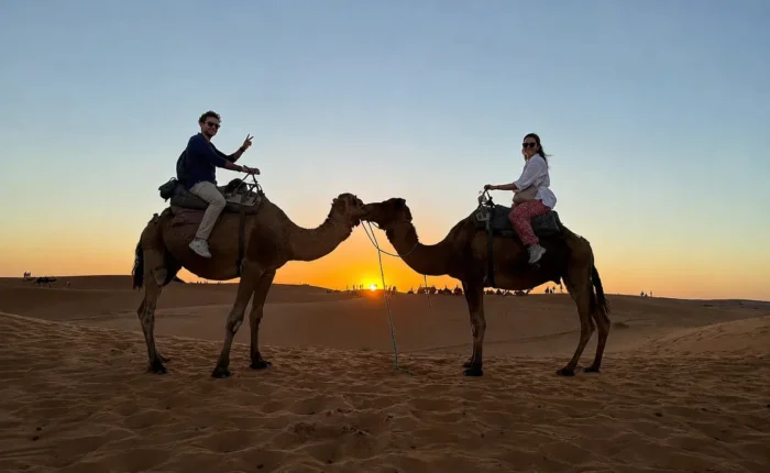 Couple riding camels at sunset in Merzouga during the 3 Days Fes to Merzouga Desert Tour