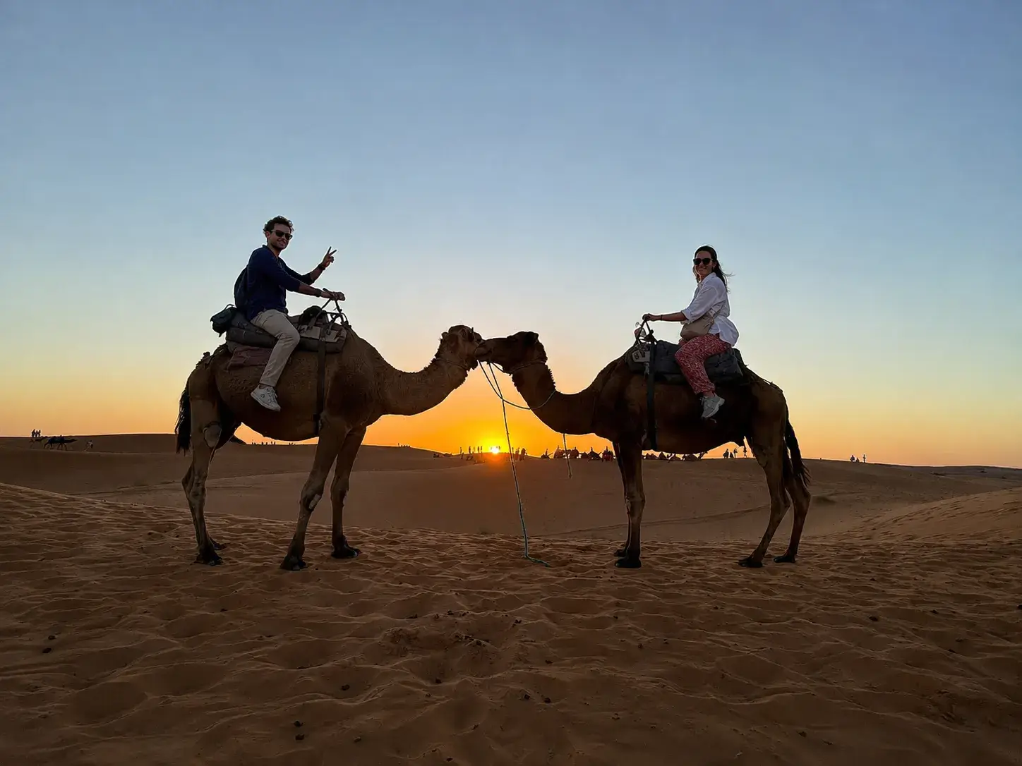 Couple riding camels at sunset in Merzouga during the 3 Days Fes to Merzouga Desert Tour